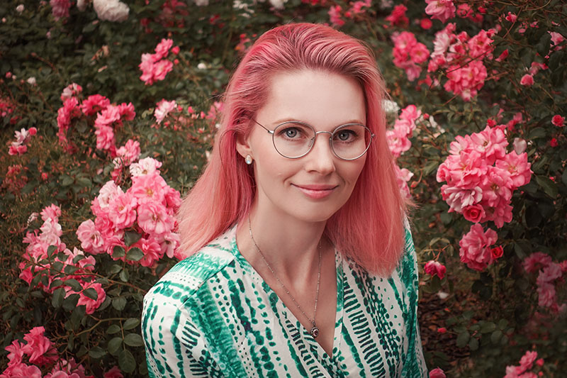 Frau mit rosa Haaren sitzt zwischen rosa Rosen